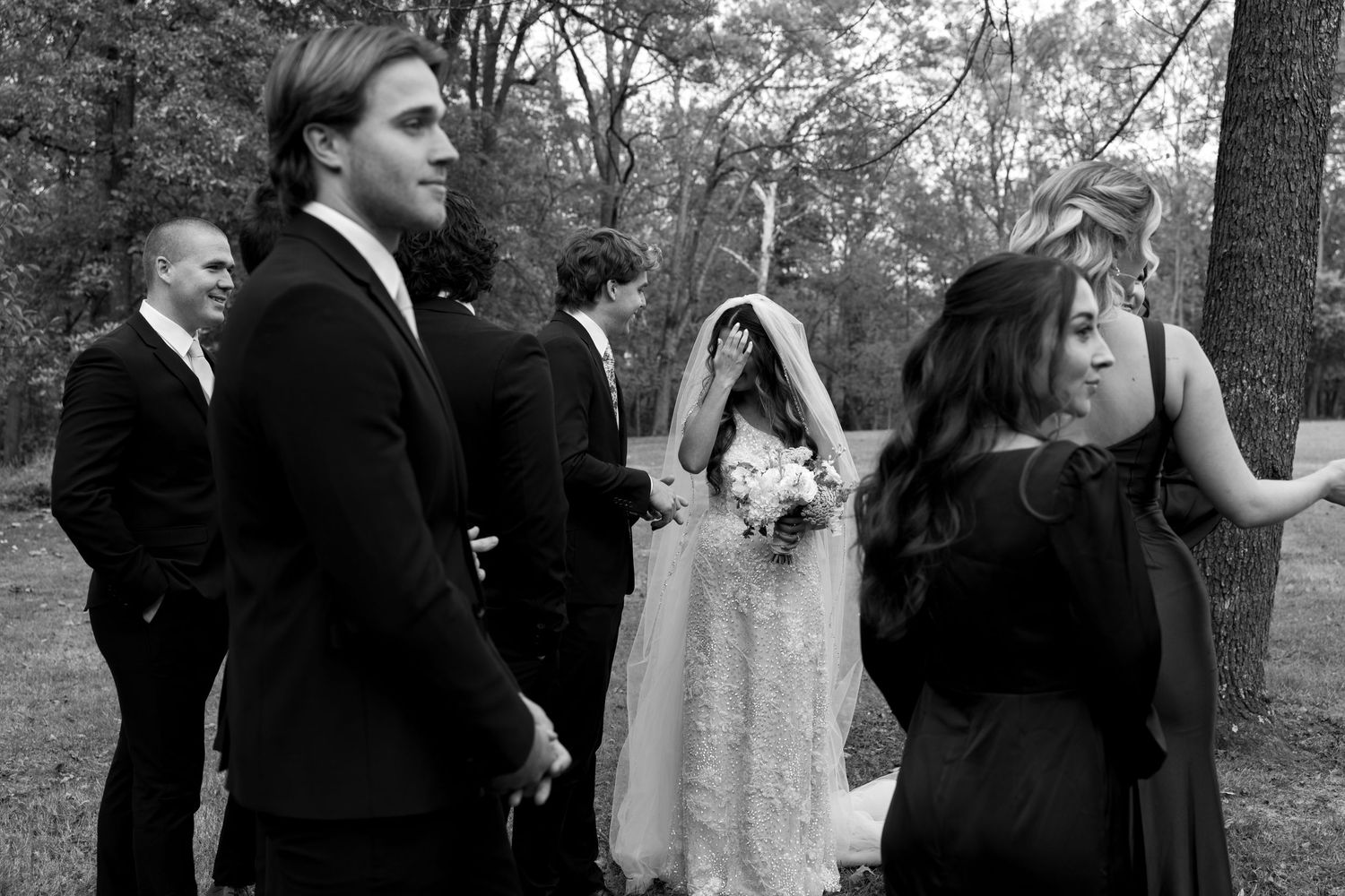 Wedding party members in formal black and white attire pose together during outdoor photo session.