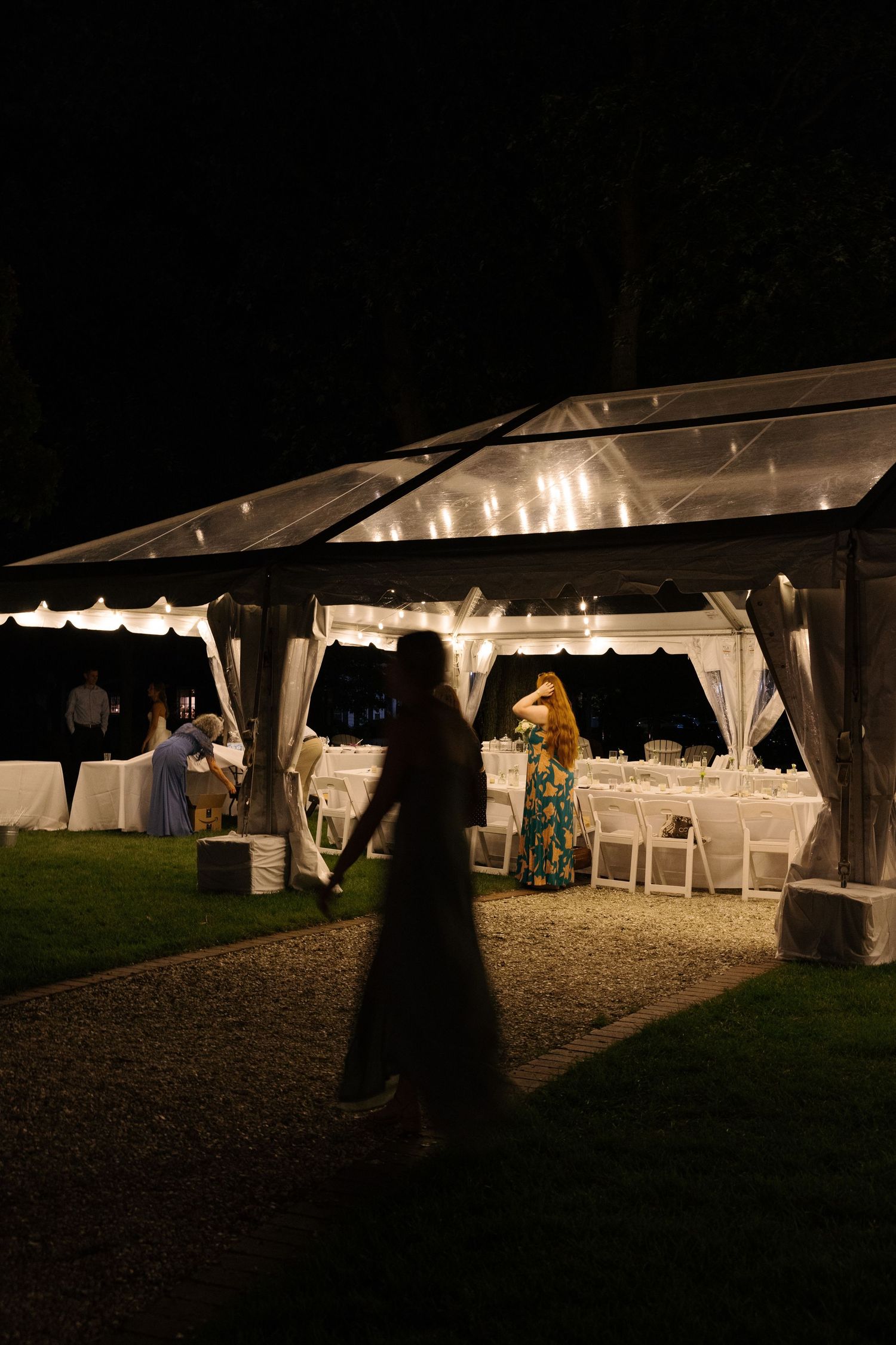 Illuminated outdoor wedding tent at night with white draping and string lights creating a romantic atmosphere.