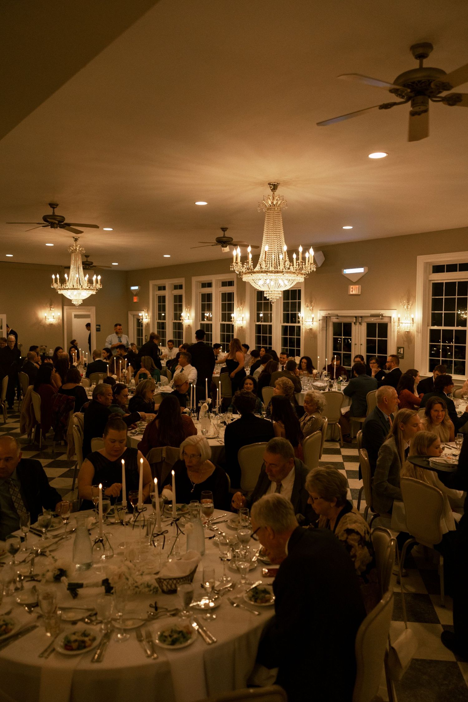 Elegant wedding reception hall with crystal chandeliers and round tables set for dinner.