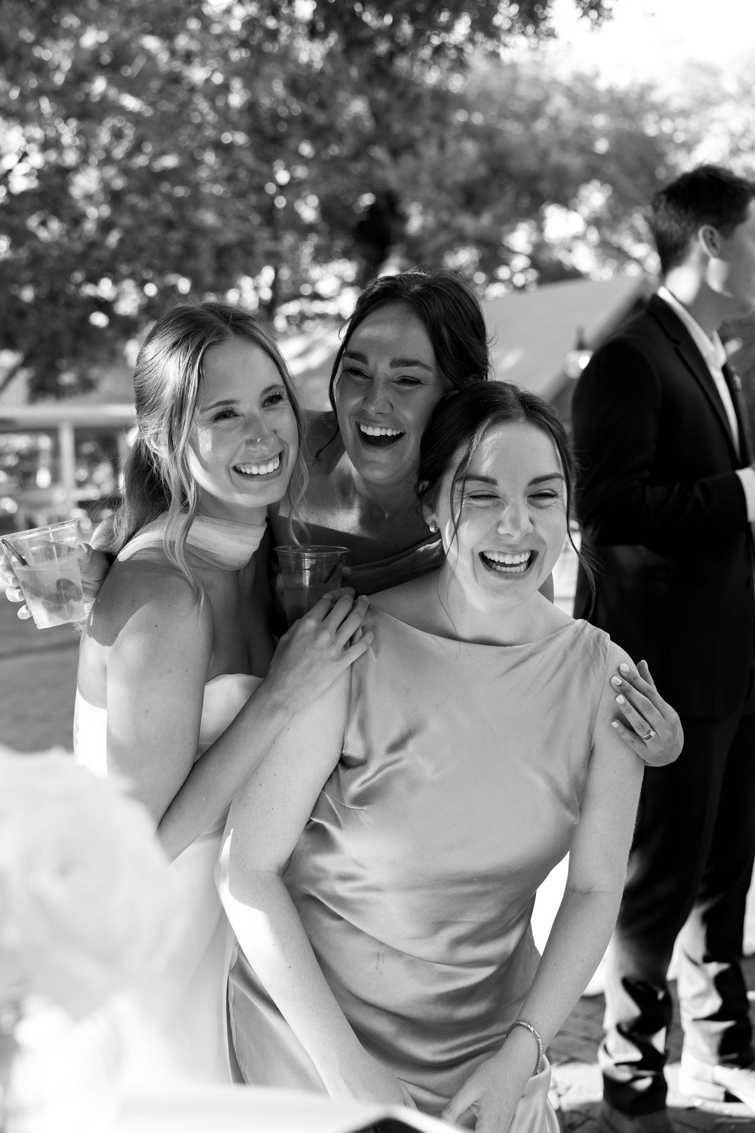 Three women laughing together joyfully at an outdoor event in black and white photography.