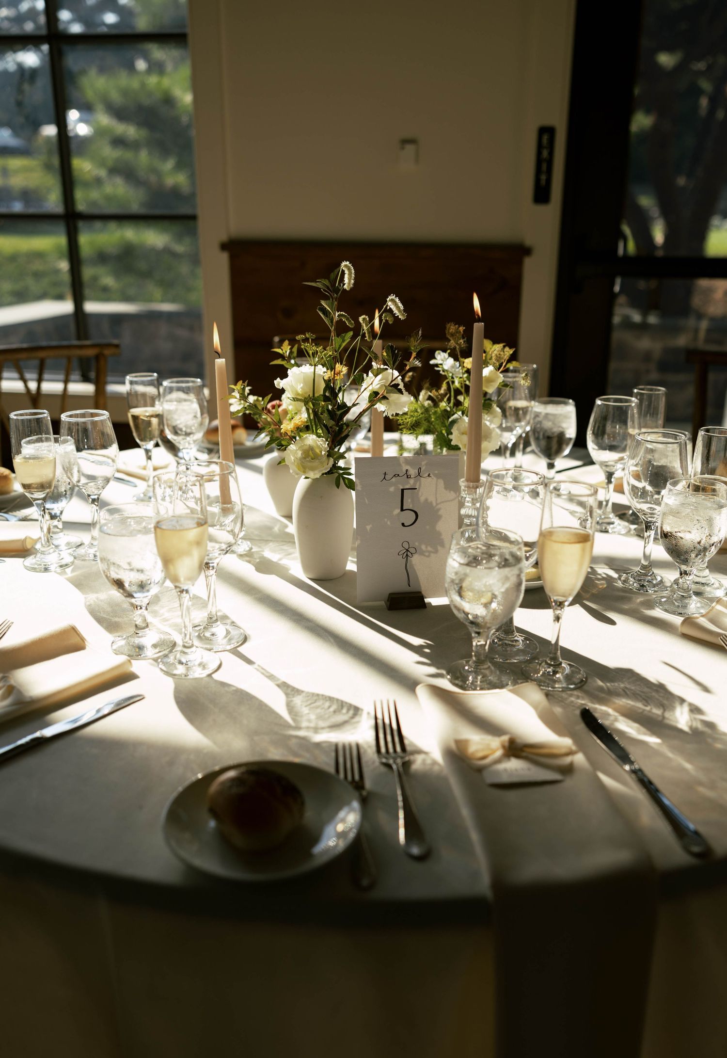Elegant wedding reception table setting with white linens, glassware, and candlelight.