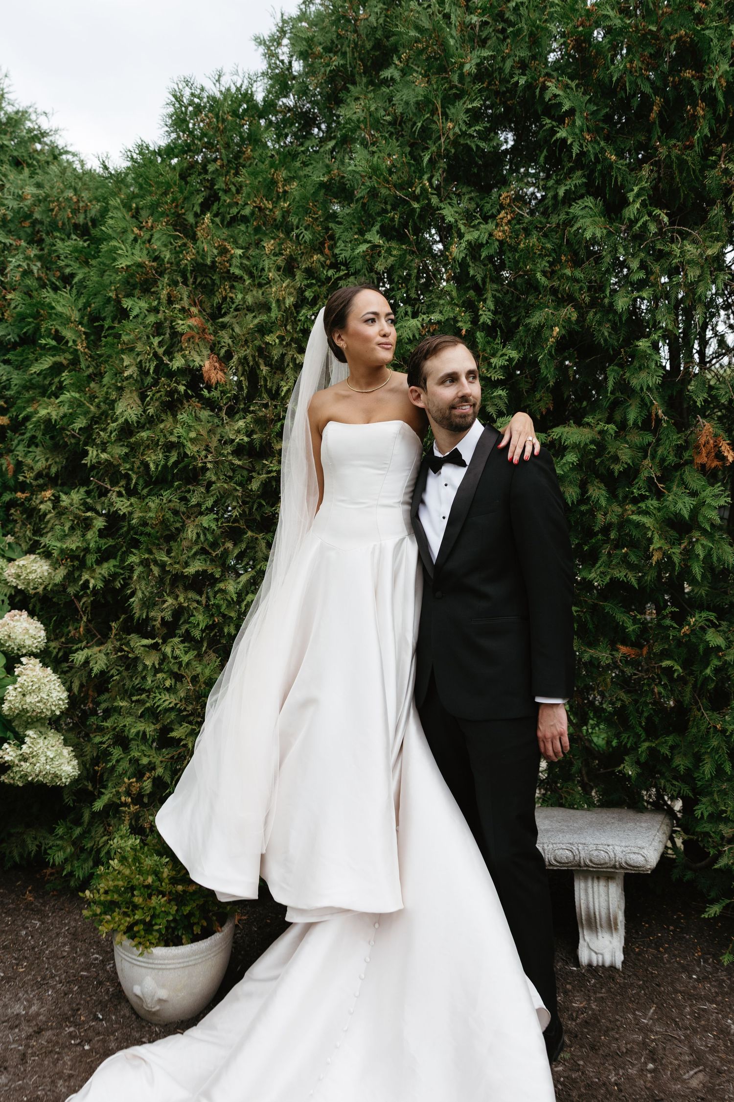 Wedding couple posing against green garden backdrop with hydrangeas.