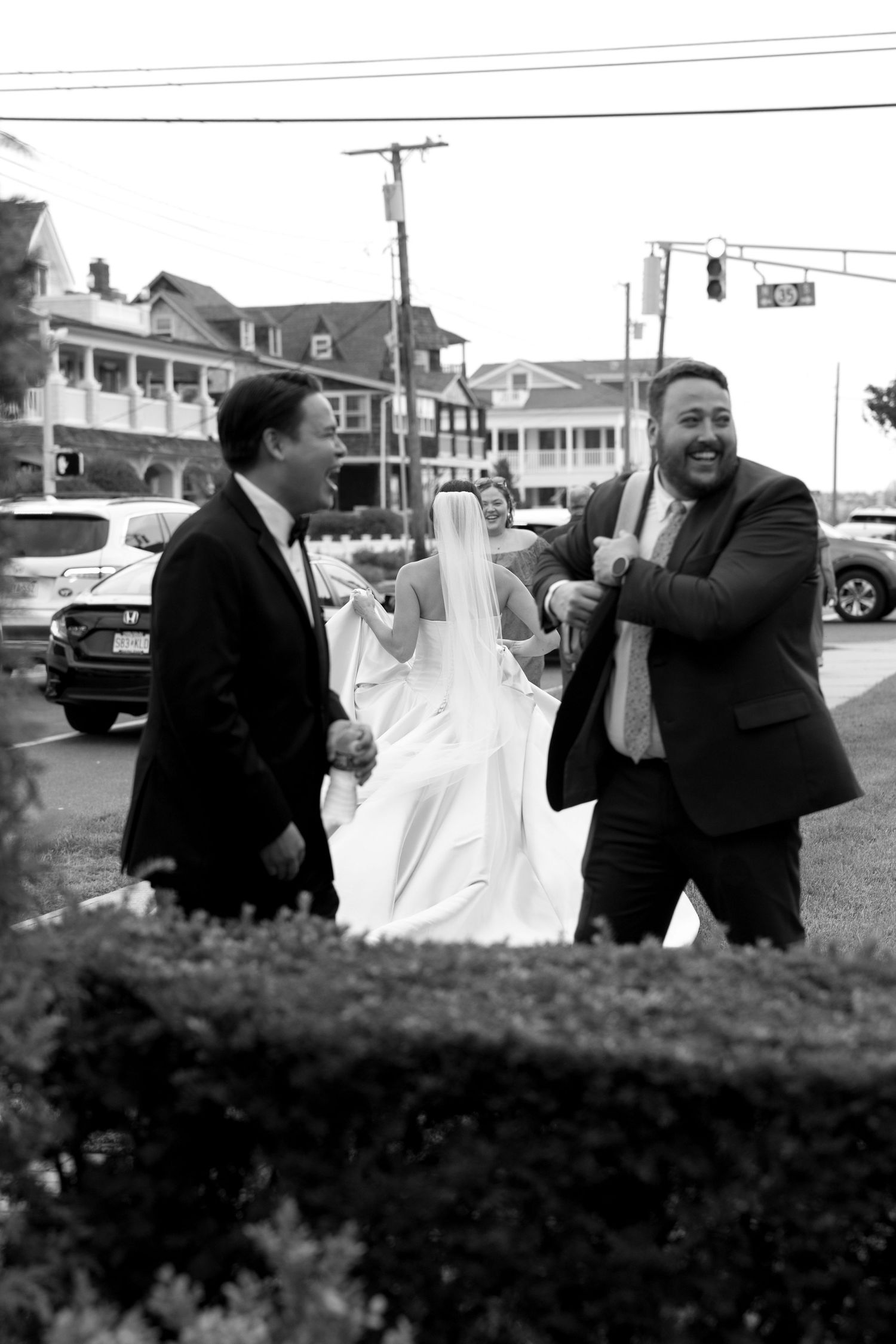 Black and white candid wedding photo taken on a street with buildings in background.