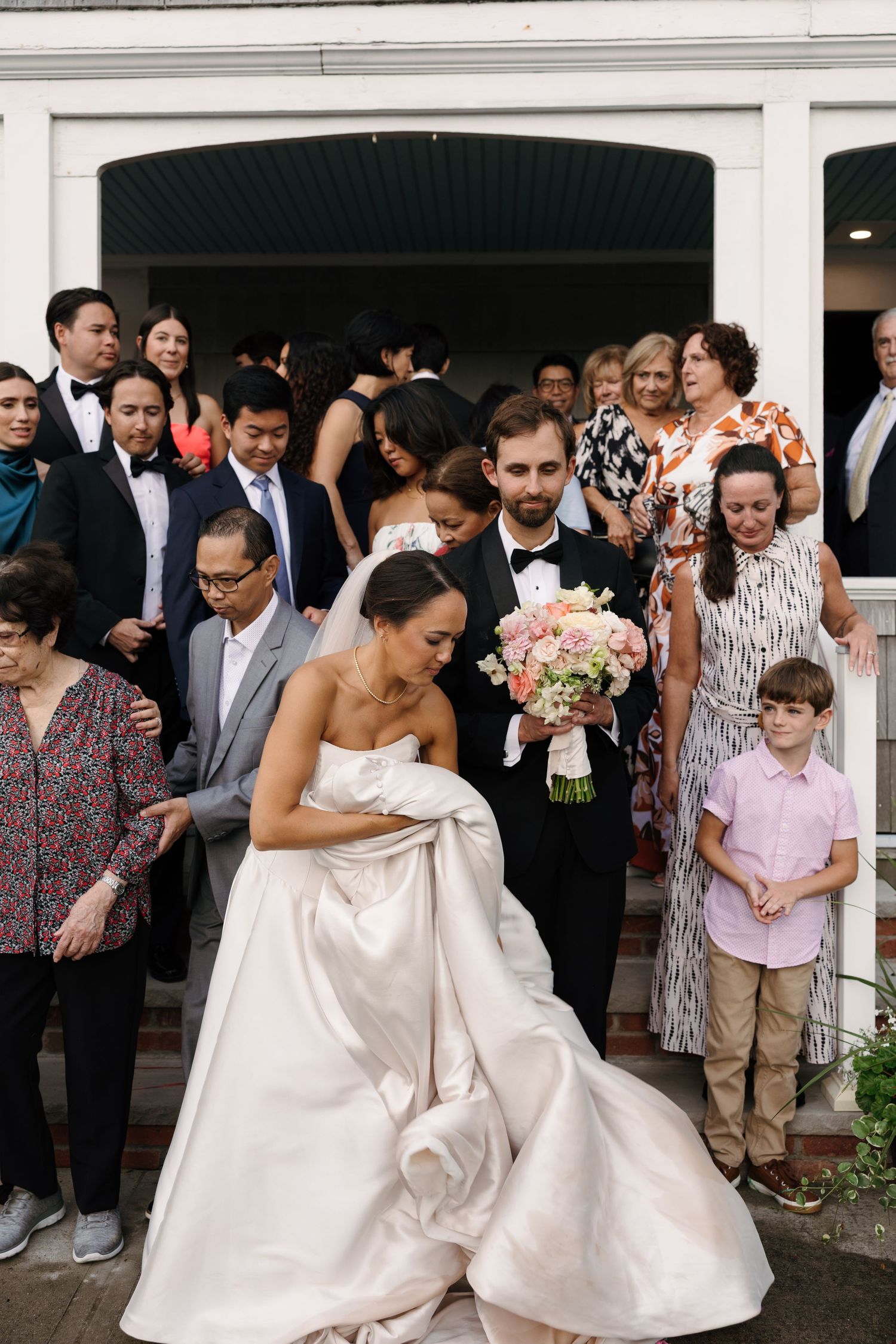 Wedding guests gather outside a white building for a celebratory moment.