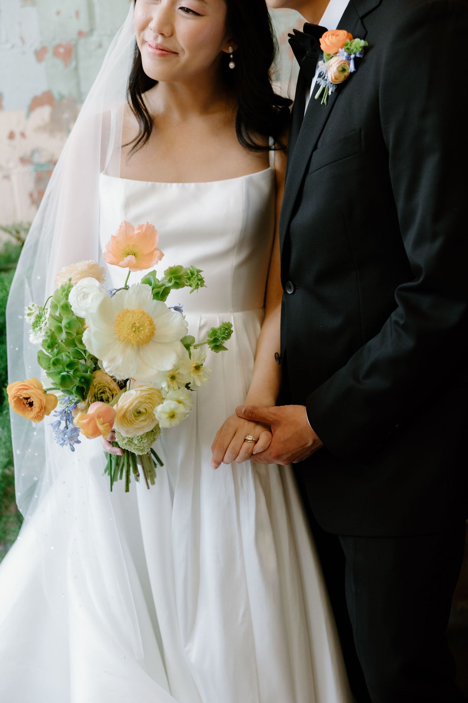 Wedding couple with a beautiful peach and white floral bouquet against a garden backdrop.