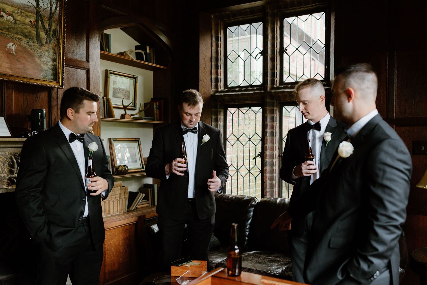 Groomsmen in dark suits toast with drinks in a dimly lit room.