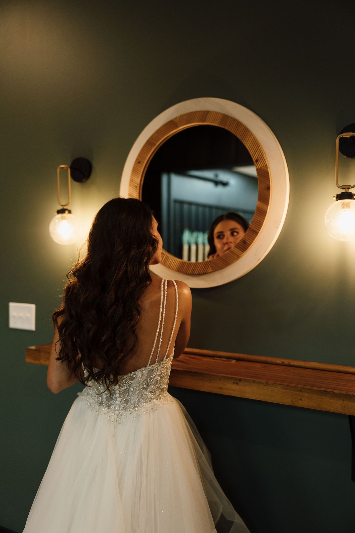 Elegant wedding dress detail with lace against a dark green wall with oval mirror.