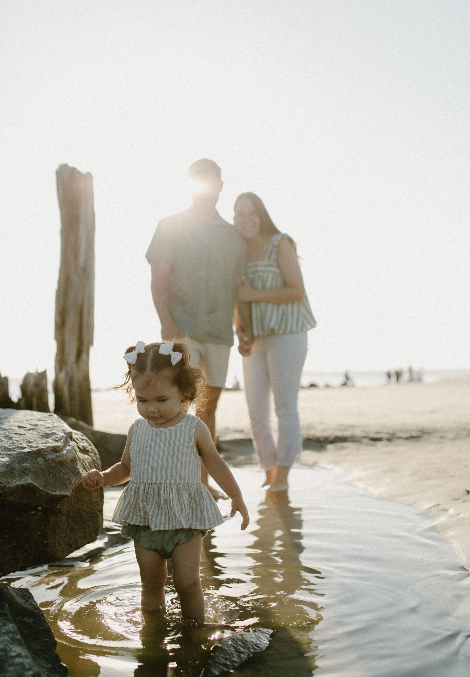 Family at beach during sunset with small child playing in shallow water.