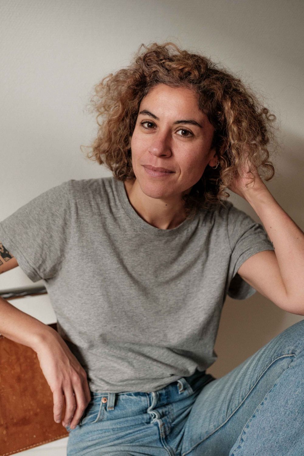 Casual portrait featuring curly hair, grey t-shirt, and relaxed pose on leather furniture.