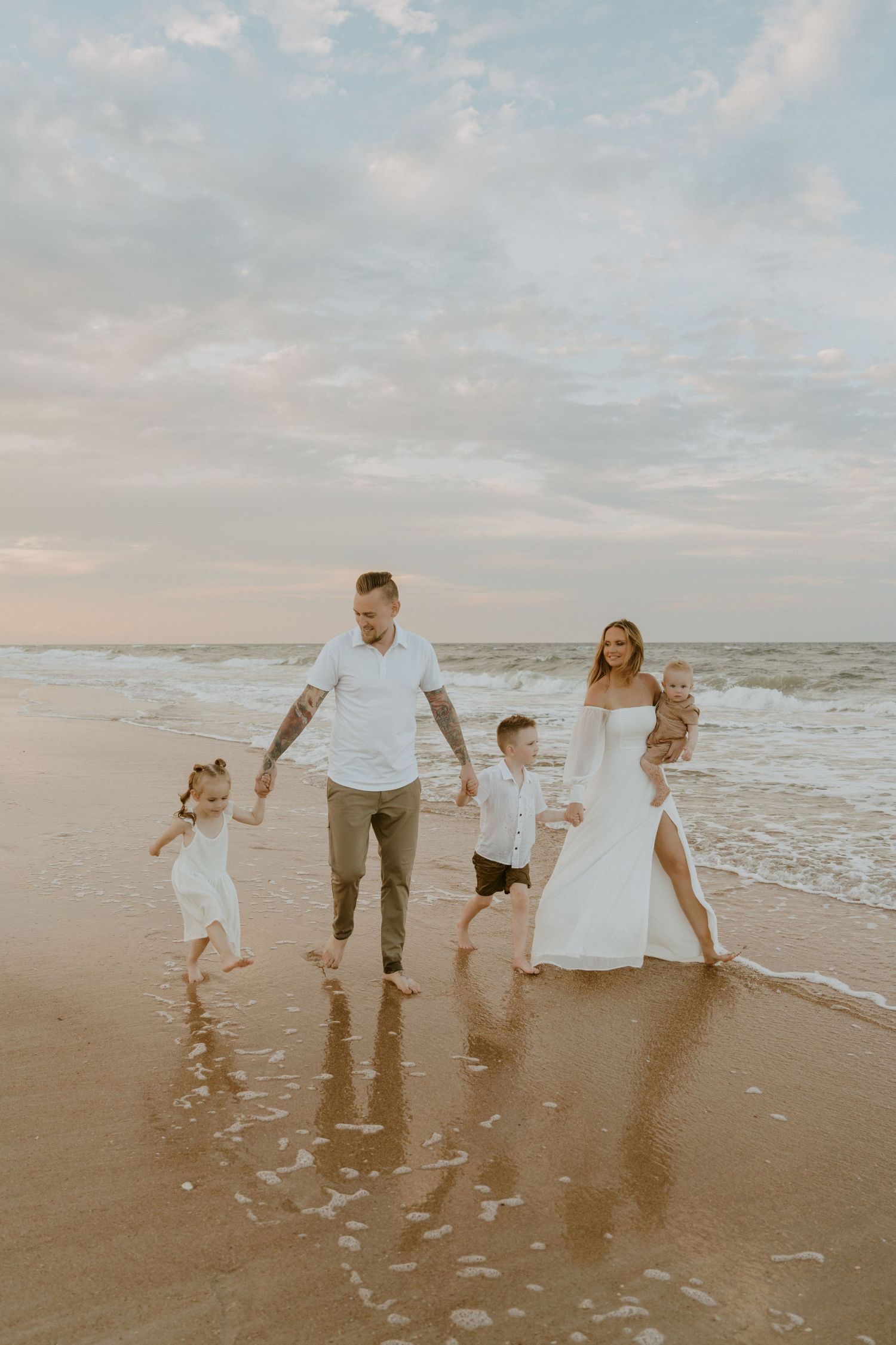 A family walks along the beach at sunset, holding hands and enjoying the ocean waves.