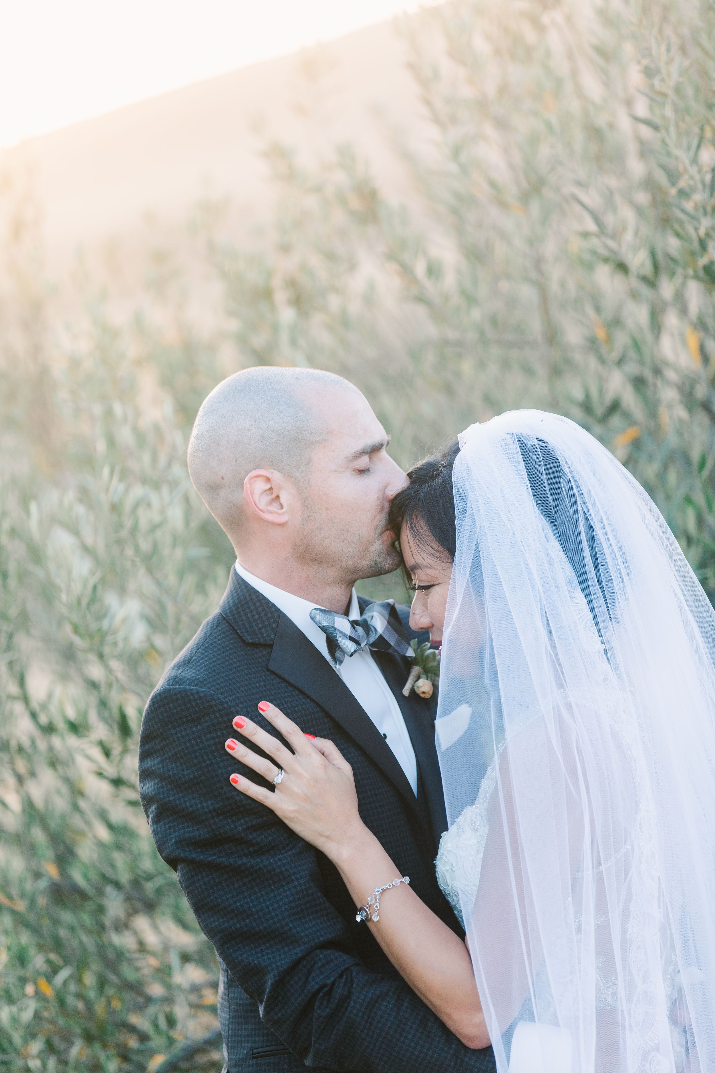 Intimate wedding portrait of couple sharing romantic moment in sunlit field.