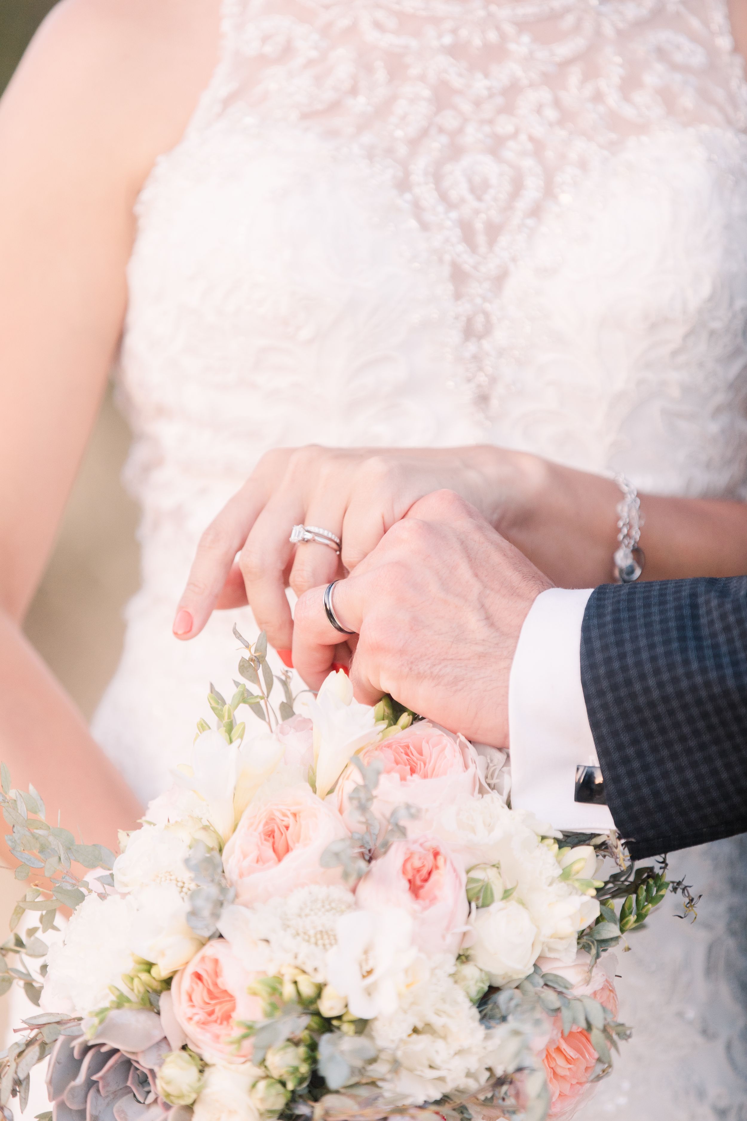 Close up of wedding rings and bridal bouquet with soft pink and white flowers.