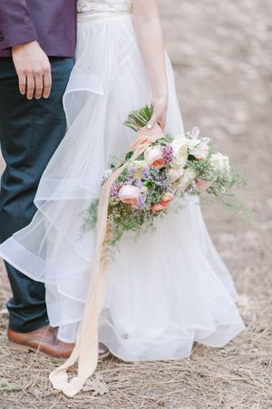 Wedding details showing white bridal gown with floral bouquet and peach ribbons cascading against rustic ground.