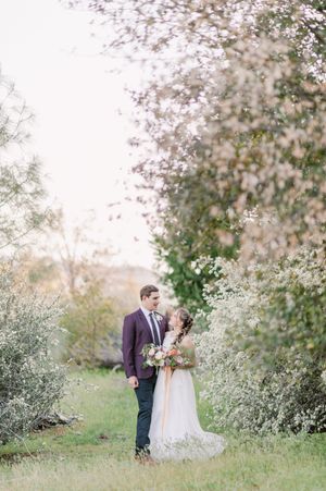 A couple embraces in an ethereal outdoor setting with delicate white blossoms and spring foliage surrounding them.