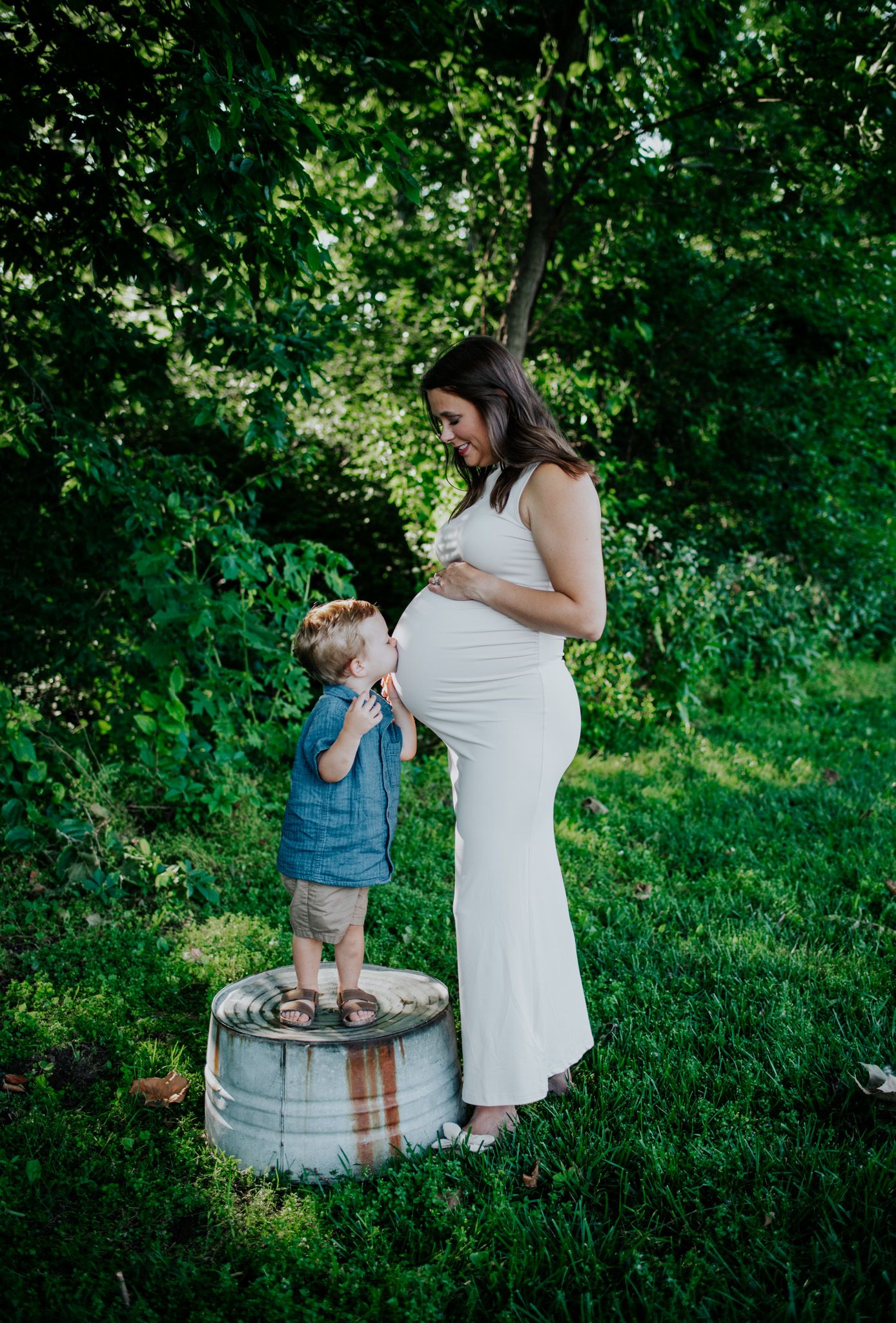 Lifestyle photos of family members playing near a rustic barrel in a lush green setting during maternity photoshoot.