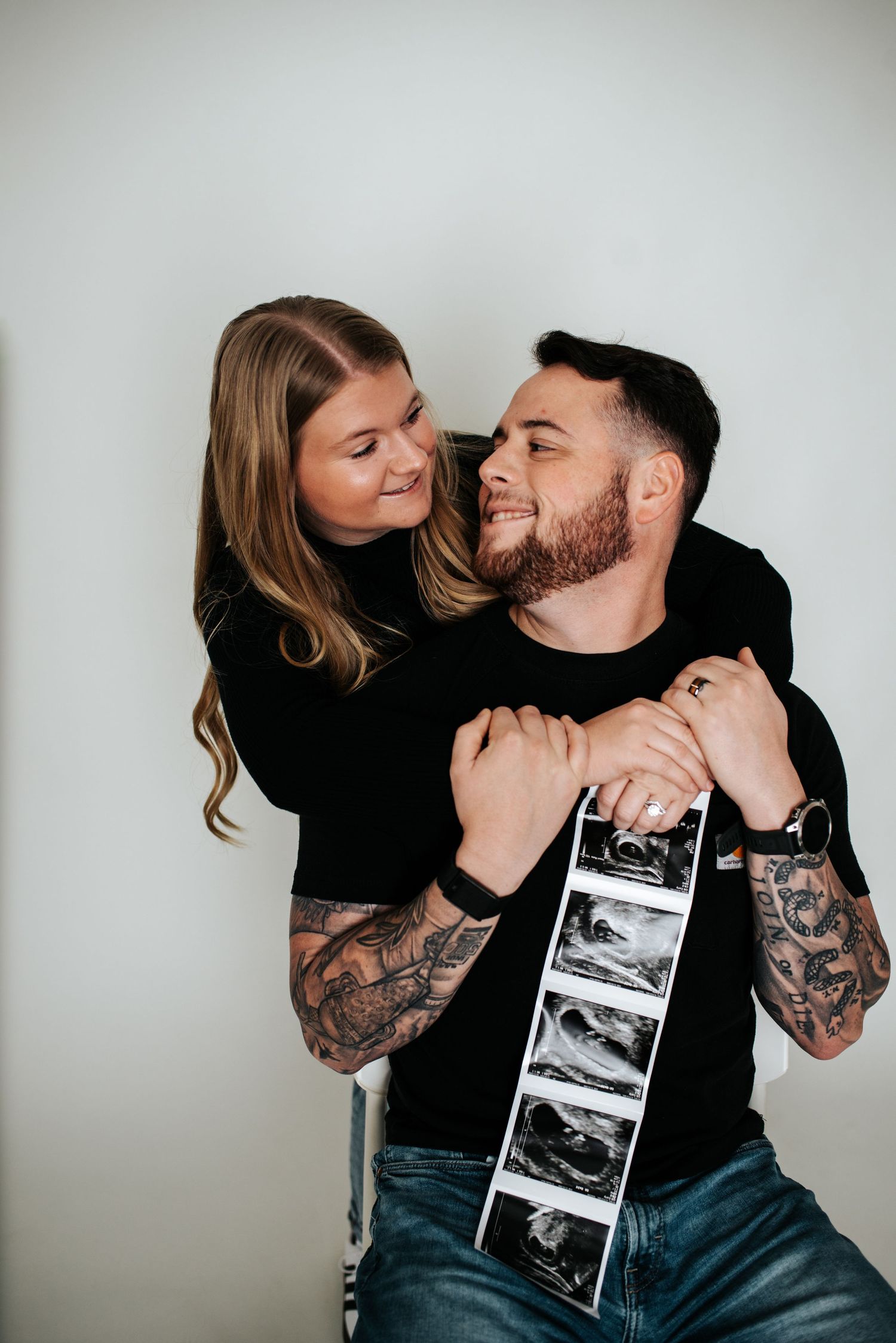Couple sharing intimate moments while holding ultrasound photos against white background.