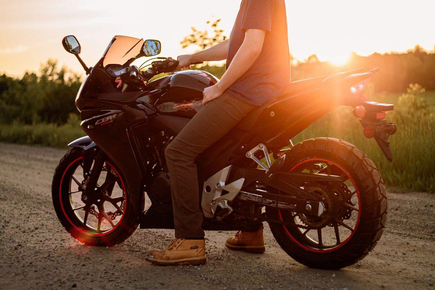 Sport motorcycle silhouetted against golden sunset with rider's boots visible on dirt road at dusk.