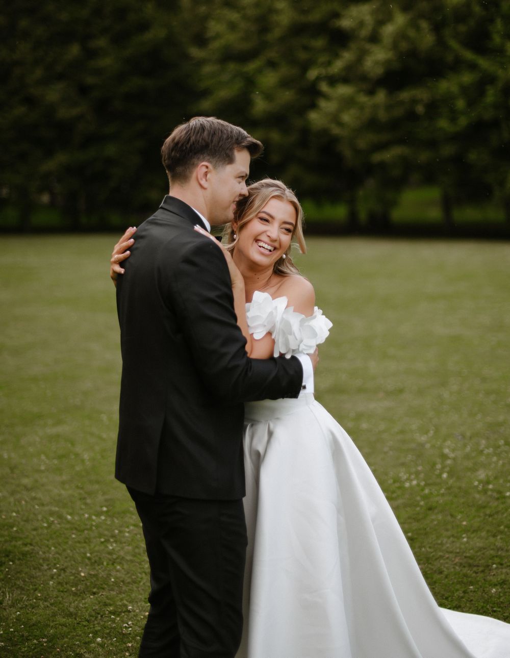 A couple shares a joyful moment together outdoors on their wedding day, with the bride in white and groom in black.