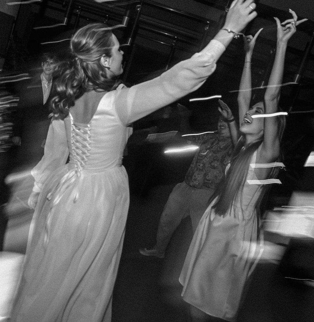Black and white photo of wedding guests dancing with raised arms at reception.