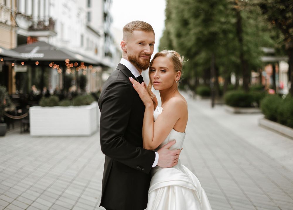 Romantic portrait of newlyweds embracing on city street with string lights in background.