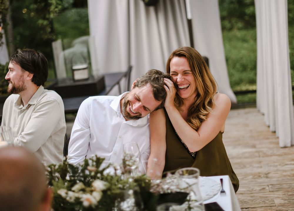 Wedding guests share joyful laughter and conversation during an outdoor reception celebration.