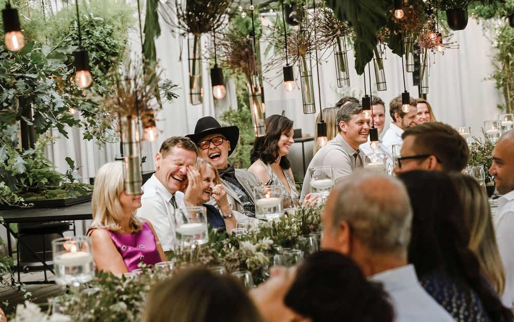 Wedding guests gather in a lush greenhouse venue decorated with hanging lights and greenery for an intimate celebration.