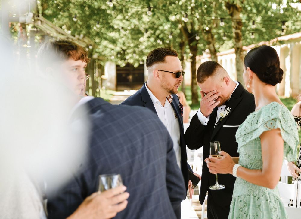 Wedding guests mingle and socialize during an outdoor reception under trees.