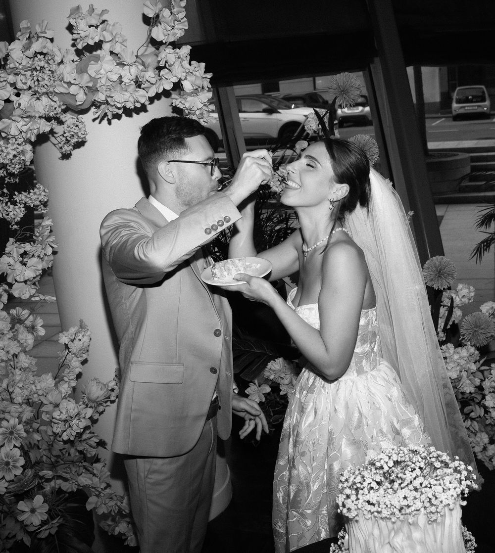 A couple in wedding attire shares a champagne toast in black and white photography.