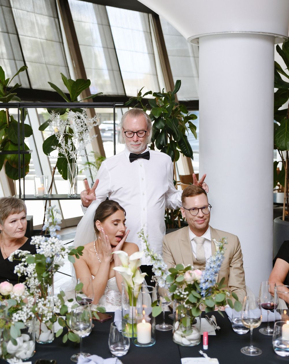 A group enjoying drinks and conversation at a bright modern venue with white columns and greenery.