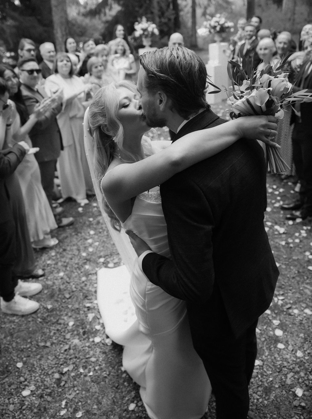 A romantic black and white wedding photo showing a couple's first dance surrounded by guests throwing flower petals.
