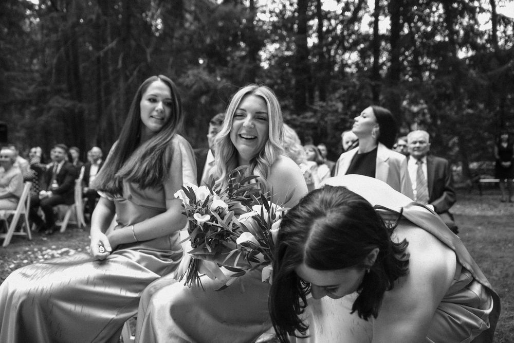 Black and white candid photo of wedding guests sharing a joyful moment during an outdoor ceremony.