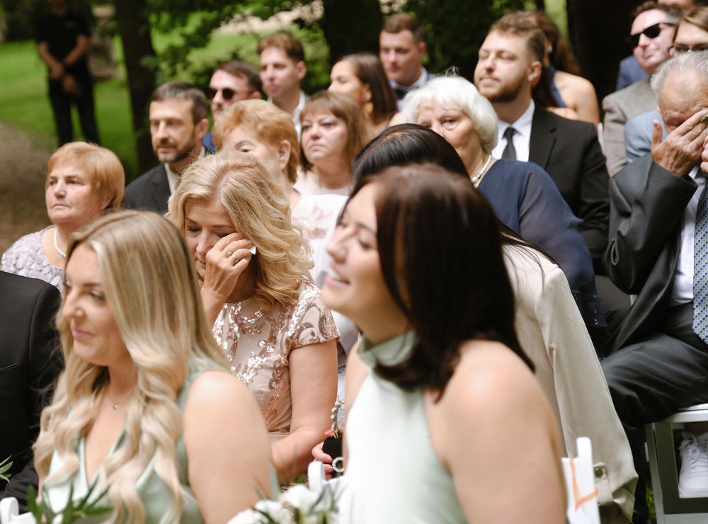 Wedding guests seated outdoors in rows of white chairs during an elegant garden ceremony.