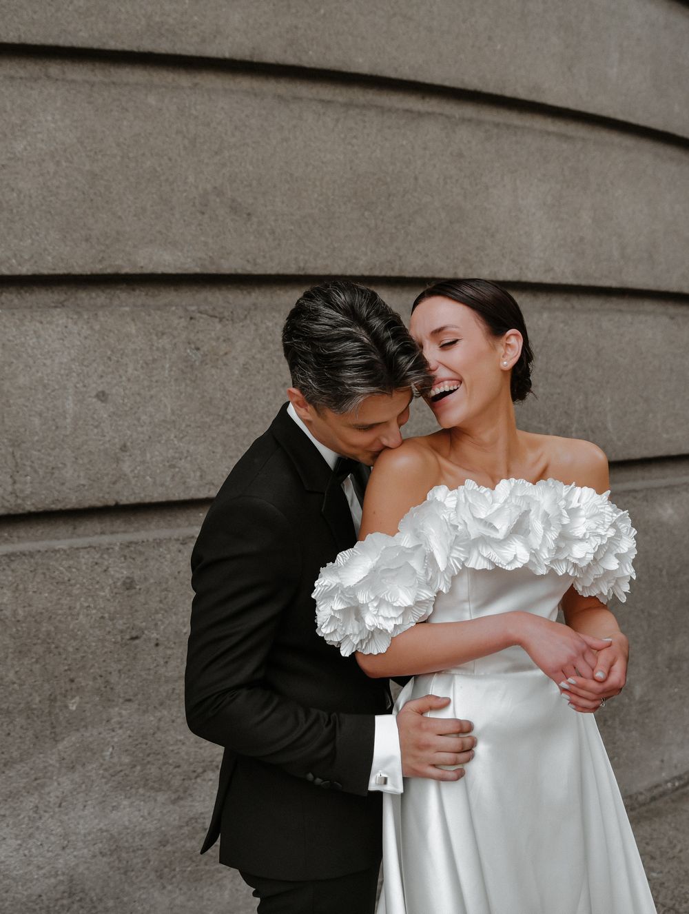 An intimate wedding moment captured against a textured wall showing affection between newlyweds.