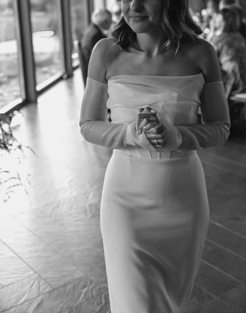 A black and white photo showing the elegant details of a fitted bridal gown with off-shoulder design.