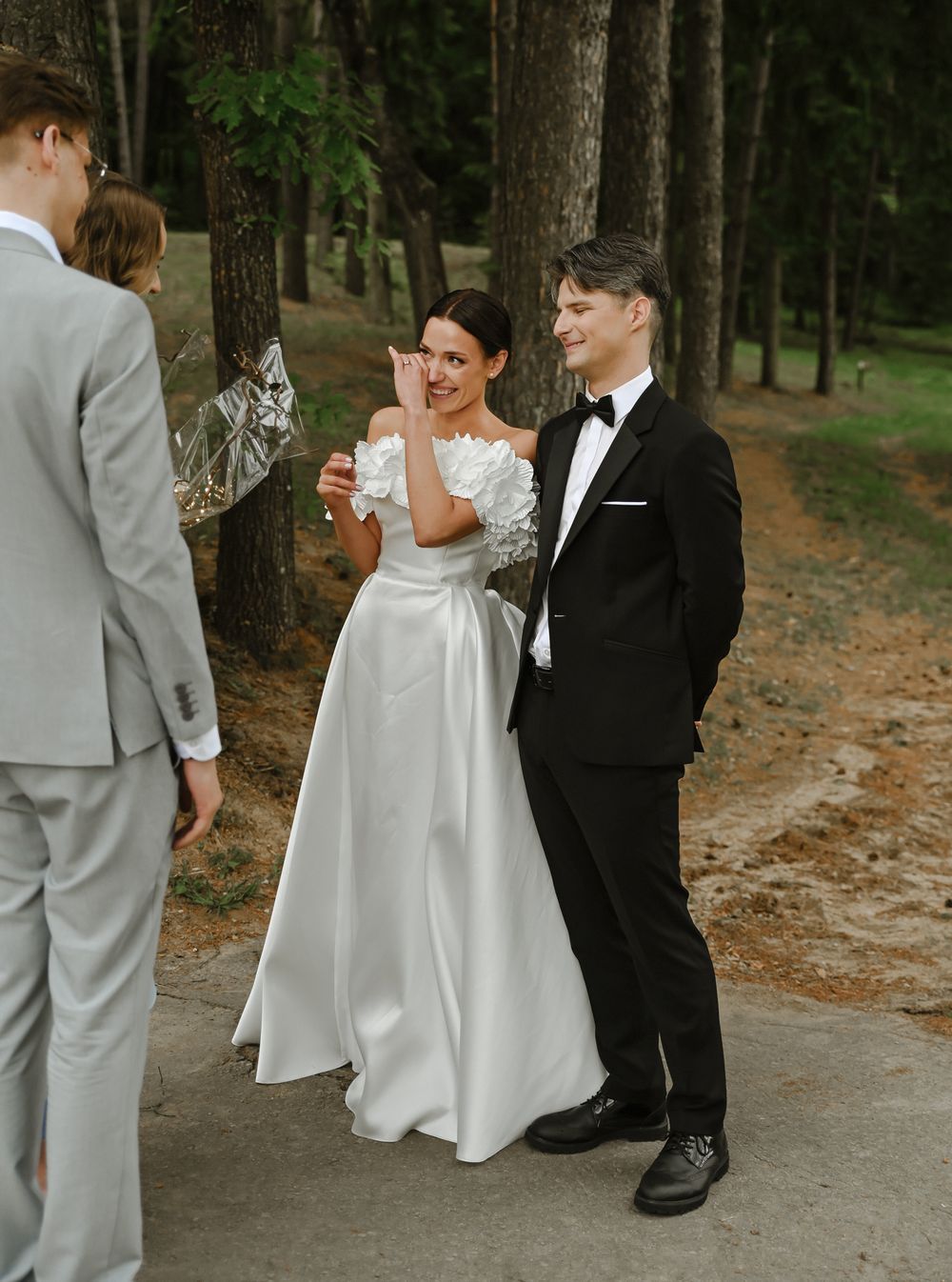 Wedding party members share laughs on a wooded path during outdoor celebration.