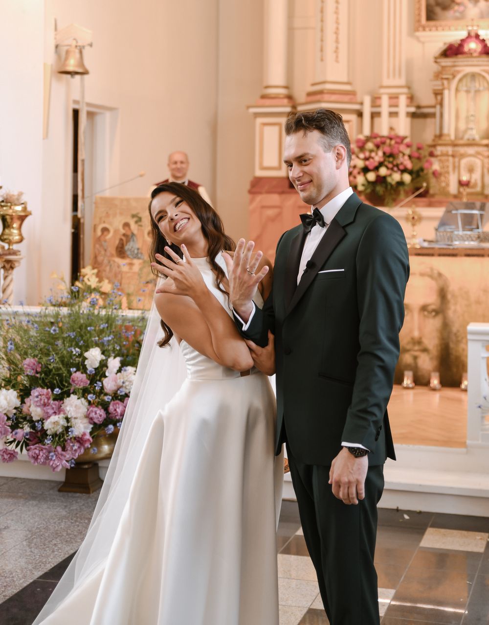 Wedding ceremony inside ornate church with pink floral arrangements.