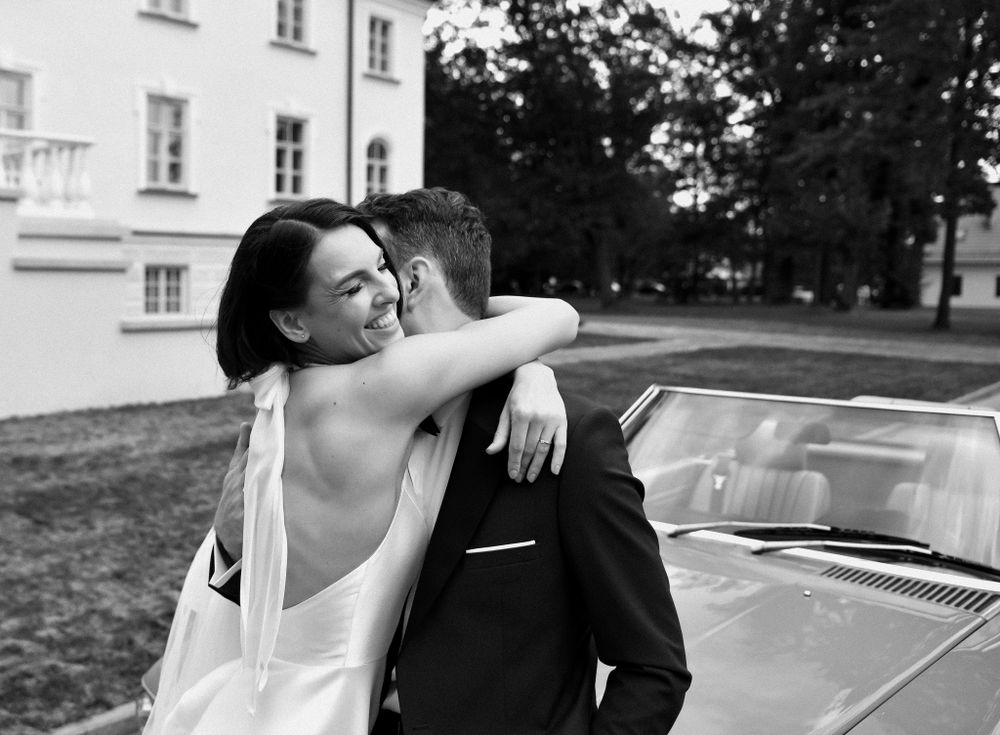 Black and white photo of couple embracing next to vintage car.