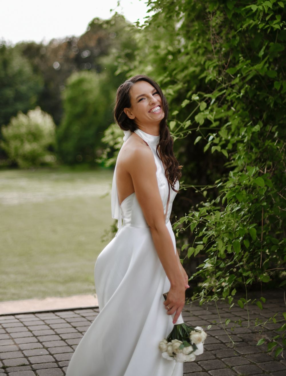 A bride in a classic white dress poses joyfully in a garden setting.