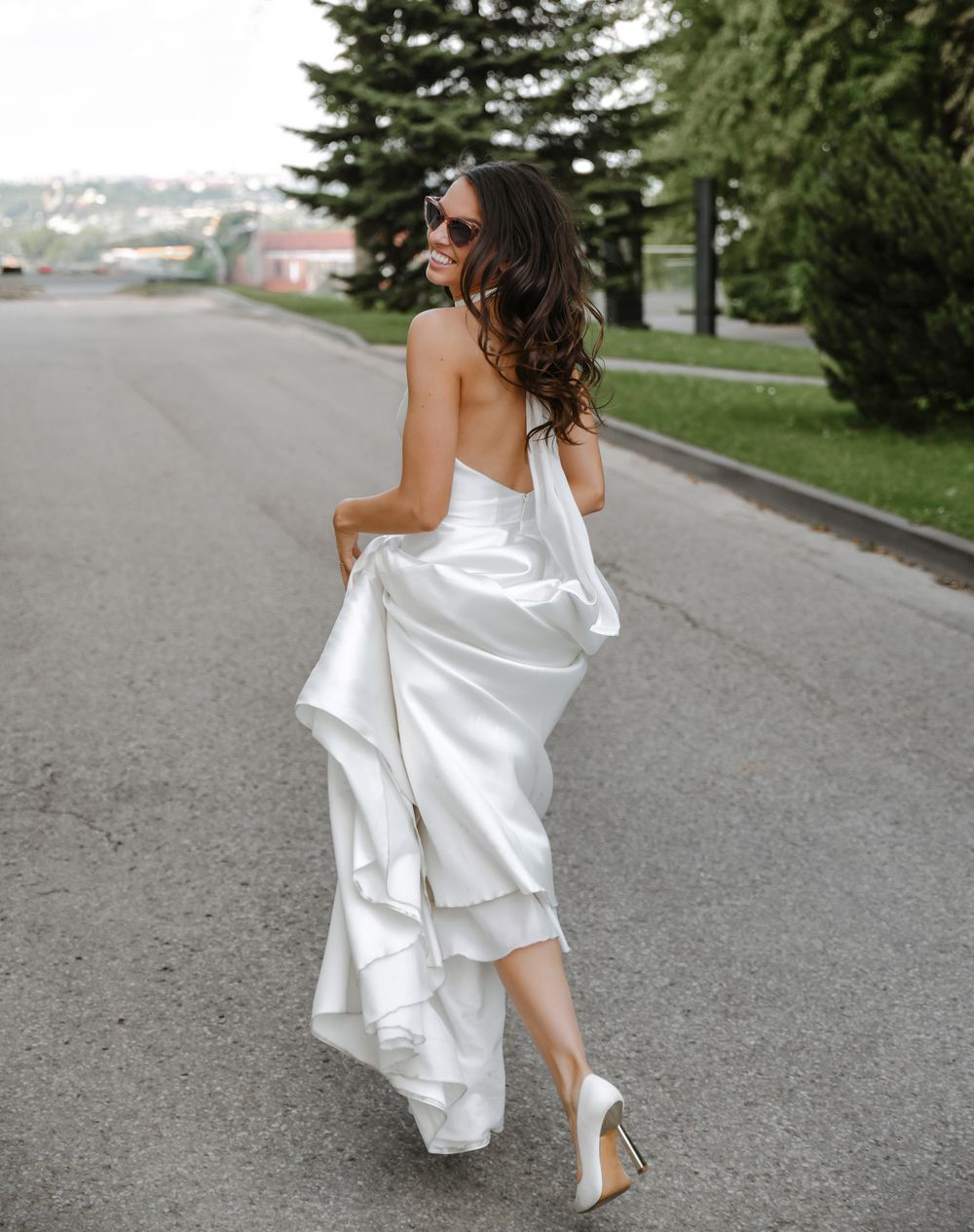 A bride in a flowing white dress walks along a path outdoors.