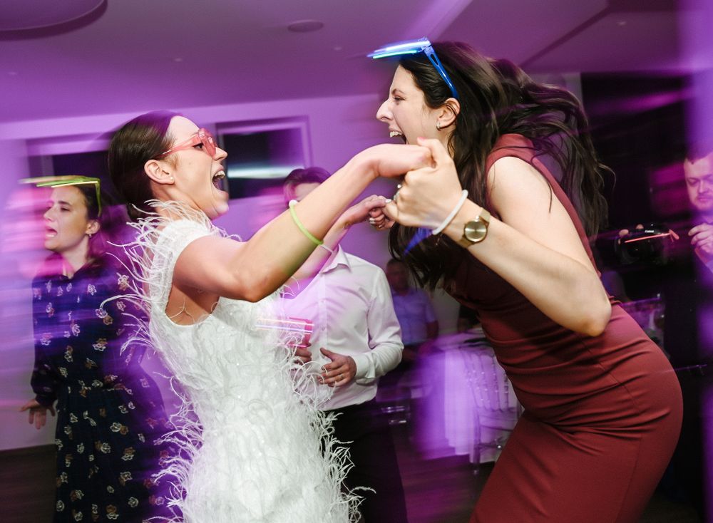 Two wedding guests sharing a playful dancing moment under purple lighting at a reception.