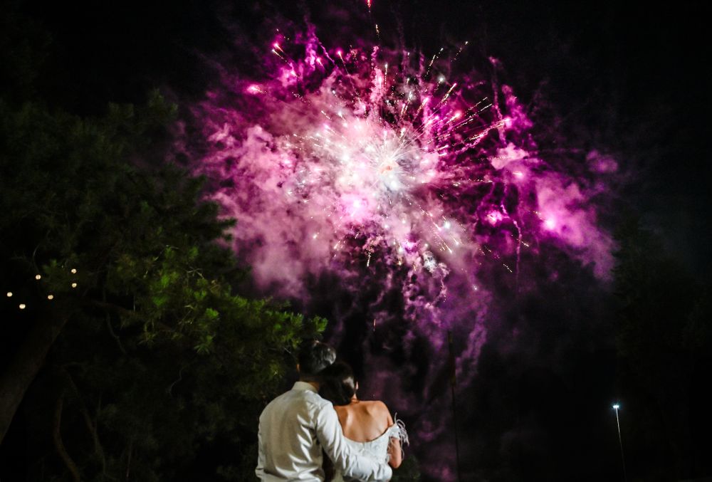 Newlyweds watching vibrant pink fireworks display during their wedding celebration.