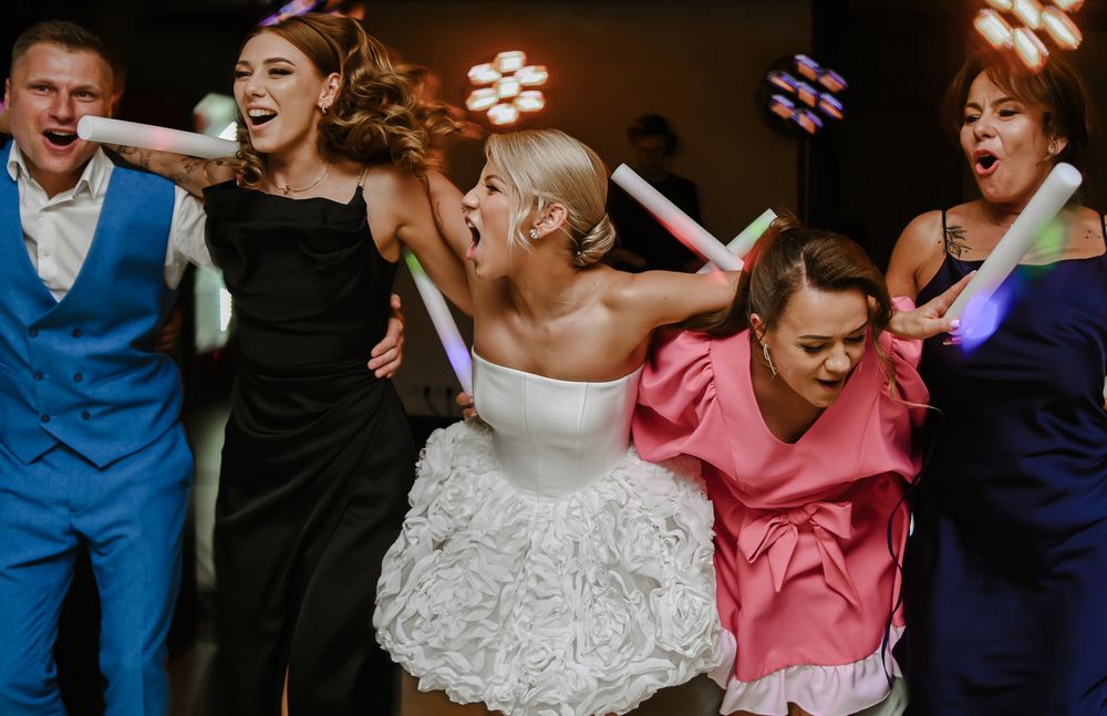 A group of wedding guests and the bride dancing energetically on the dance floor at a reception celebration.