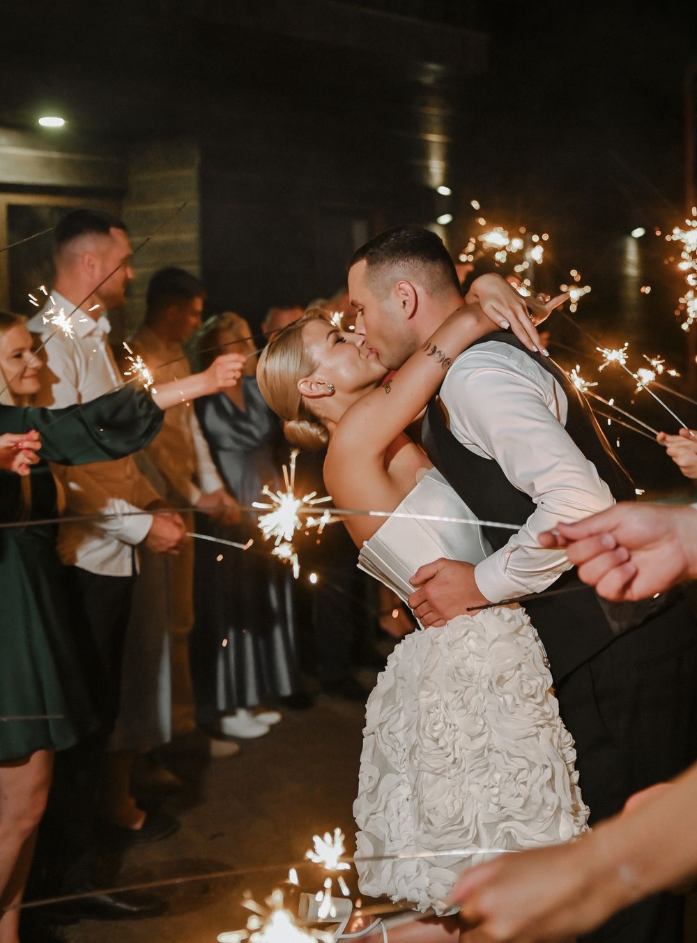 Newlyweds and wedding guests dip and dance while holding sparklers during an intimate reception celebration.