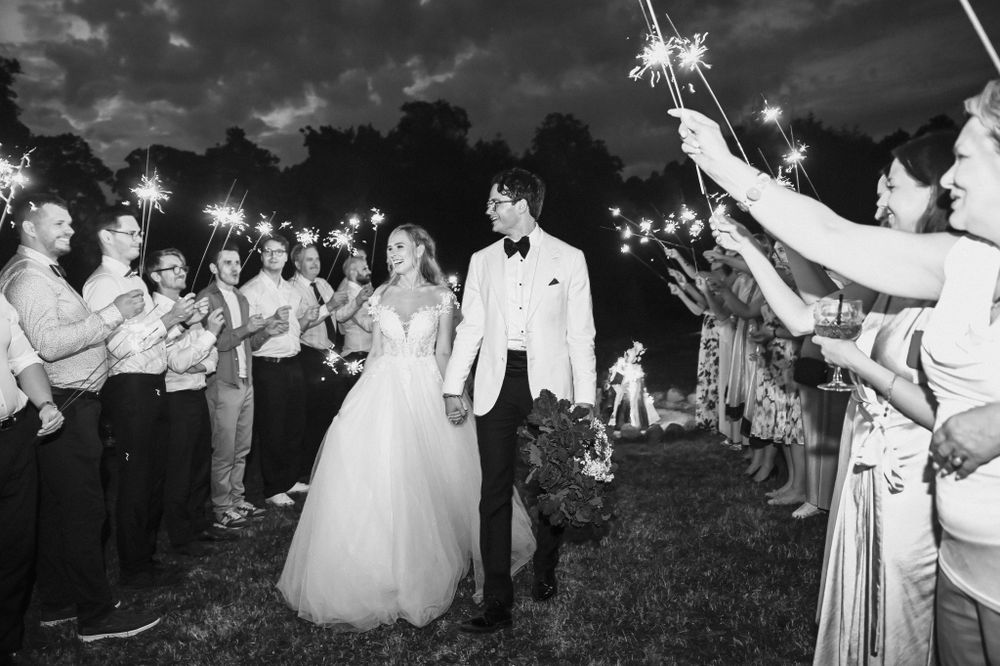 Newlyweds walk through a sparkler exit line at their wedding reception during twilight.