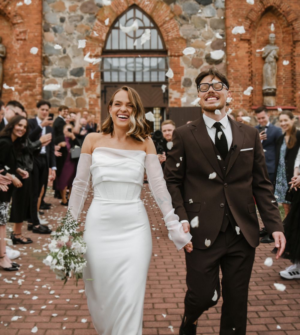 A couple celebrates during their wedding ceremony with guests throwing confetti at historic brick church building.