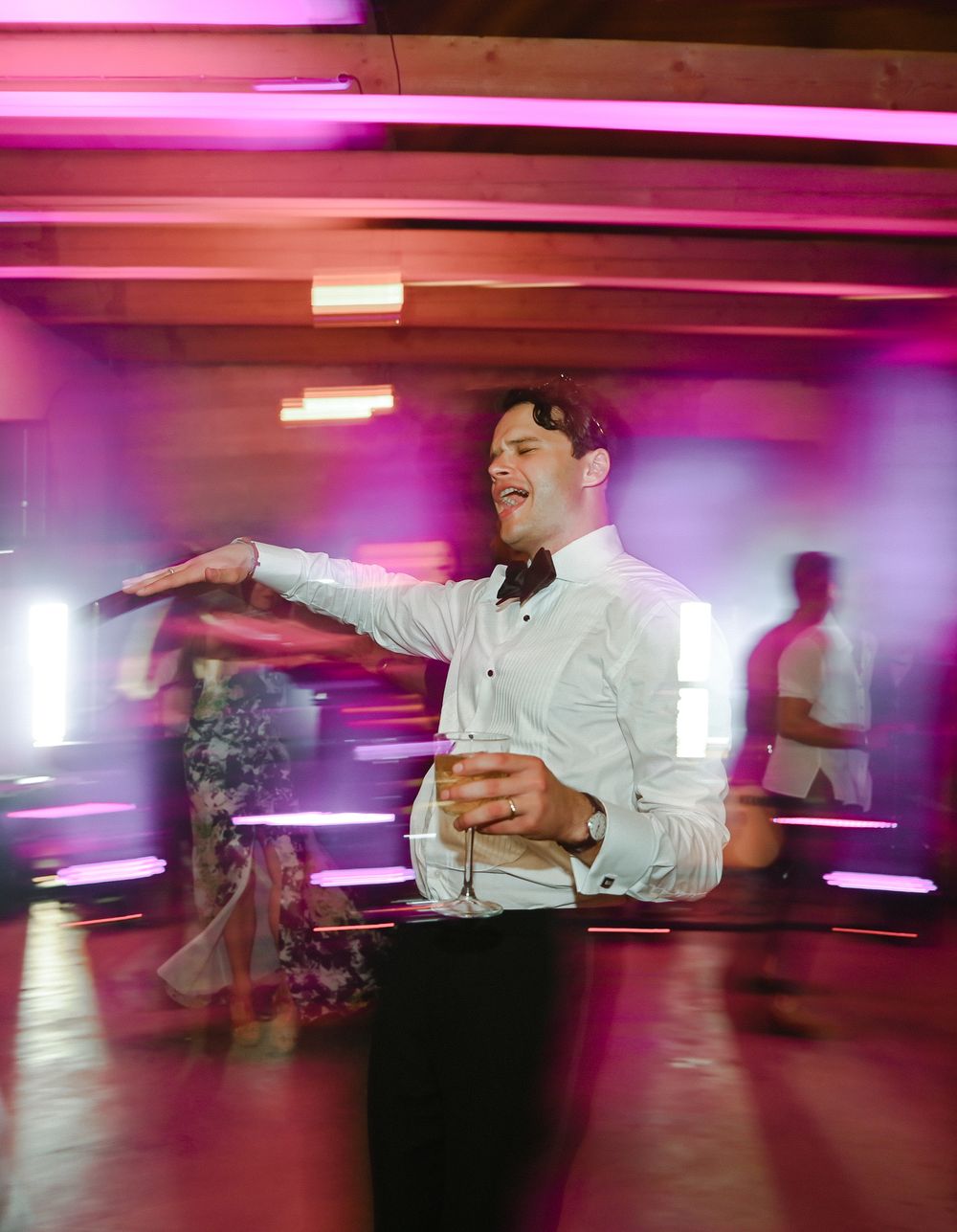Person dancing at reception with pink and purple lighting effects.