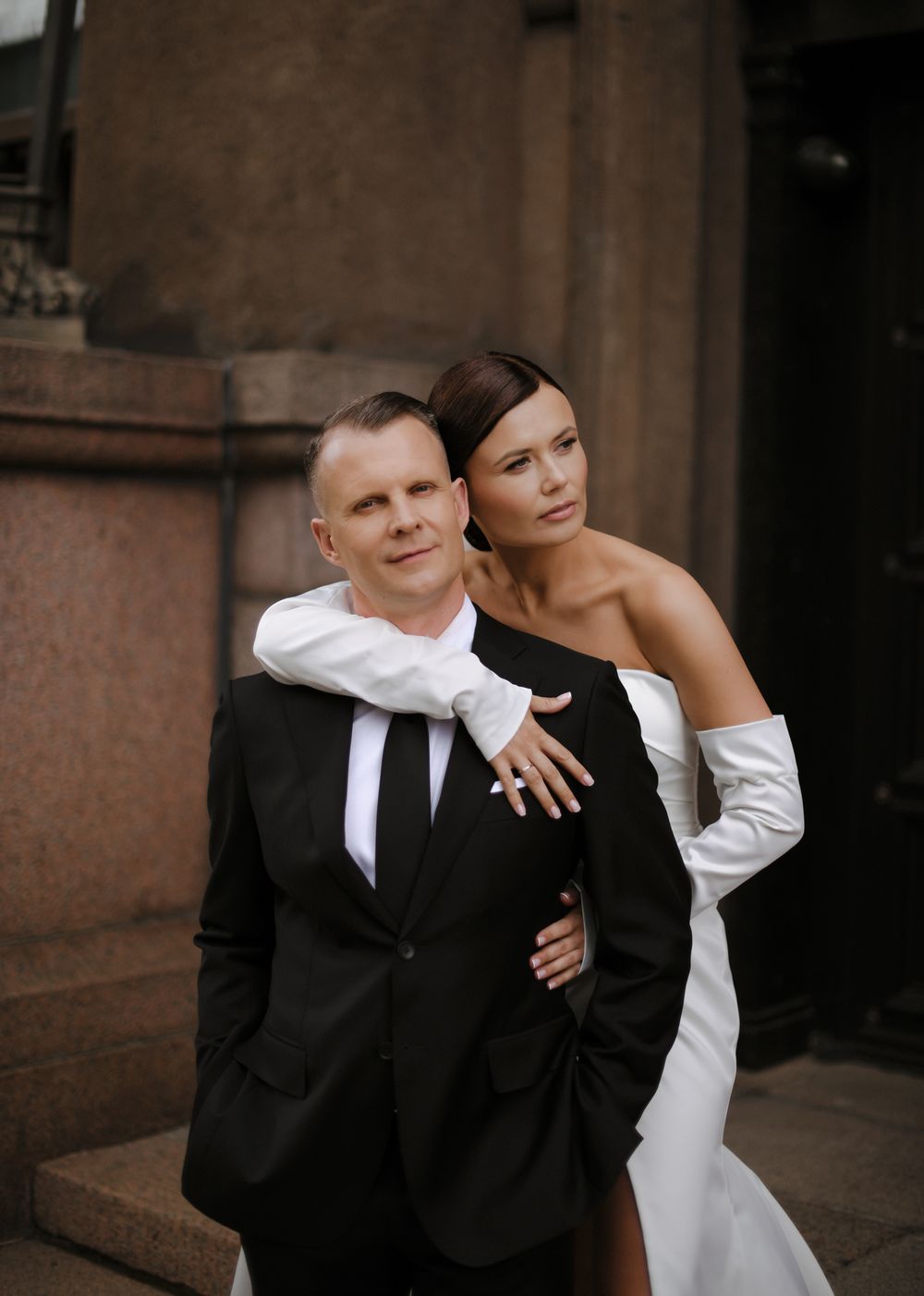 Stylish wedding portrait against stone building exterior.