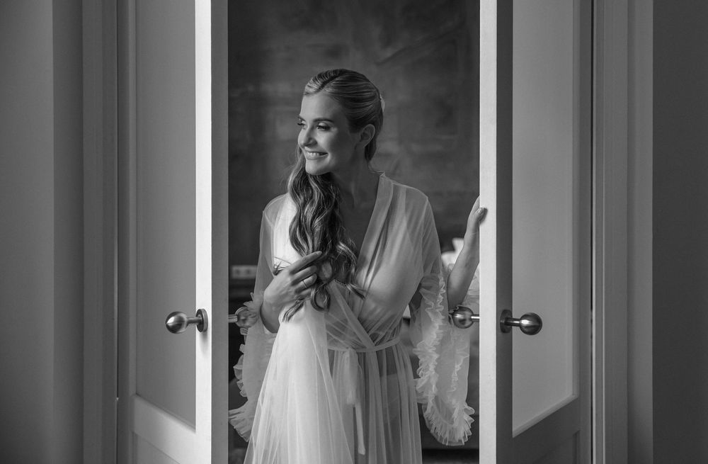 A black and white photograph of someone in a flowing dress standing in a doorway casting dramatic shadows.