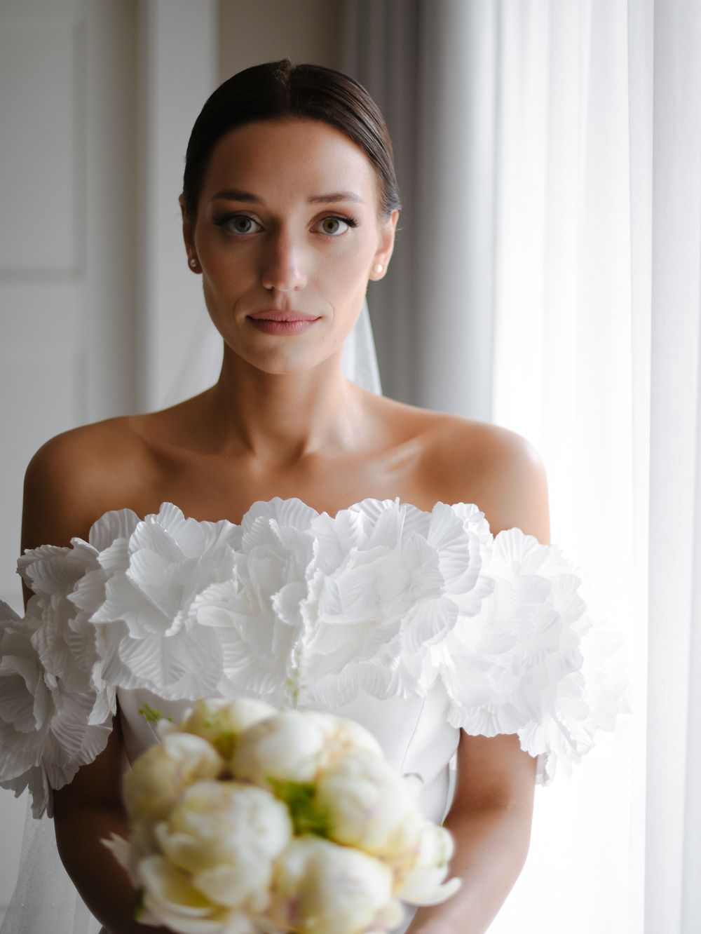 An elegant bridal portrait featuring an off-shoulder dress with ruffled details and white bouquet.