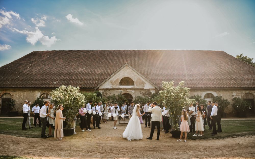 A rustic barn wedding ceremony with guests gathered outside under a warm sunset.
